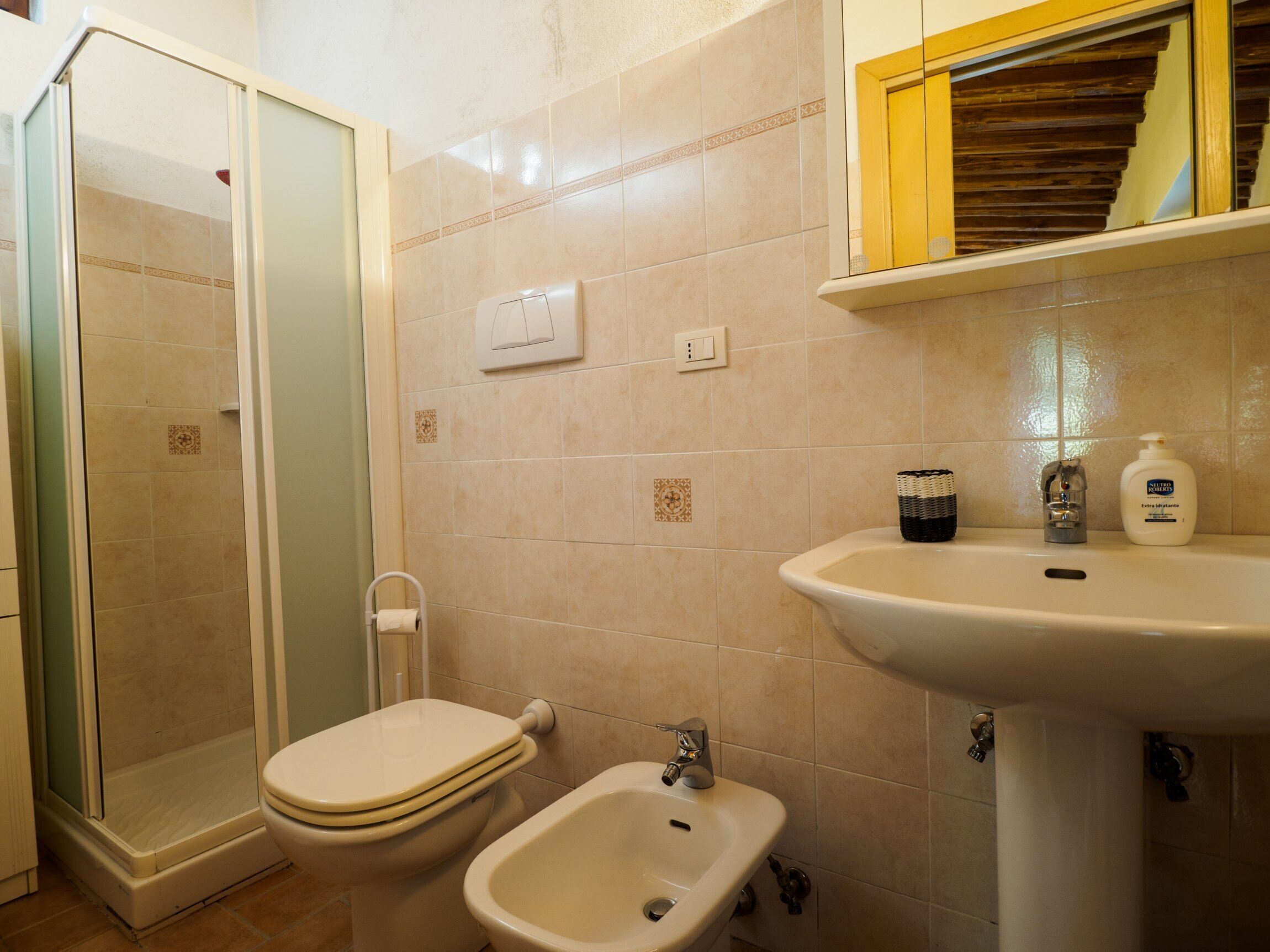 Une salle de bain équipée d’une douche, de toilettes, d’un bidet, d’un lavabo et d’une étagère où sont rangés les articles de toilette.