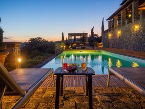 Zona junto a la piscina con mesa y sillas, un muro de piedra y vistas a la piscina.