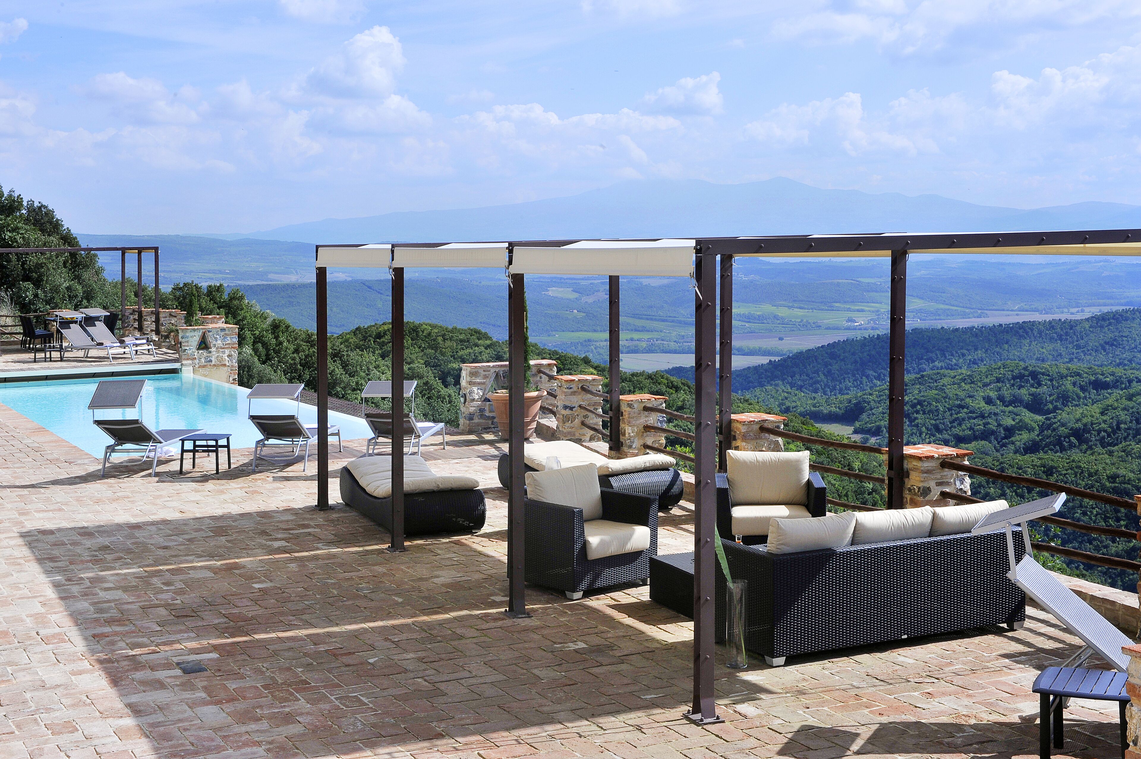 A rooftop terrace with a pool, lounge chairs, and a view of a mountainous landscape.
