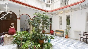 A courtyard with a checkered floor, potted plants, a wooden bench, and a balcony with white railings. - La Herencia del REGIDOR by Cadiz4Rentals (Cádiz)