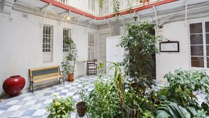 A spacious courtyard with a checkered floor, a wooden bench, potted plants, and a balcony with hanging plants. - La Herencia del REGIDOR by Cadiz4Rentals (Cádiz)