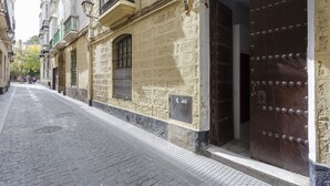 A narrow cobblestone street with historic buildings, a large wooden door with metal studs, and a small window with a barred design. - La Herencia del REGIDOR by Cadiz4Rentals (Cádiz)