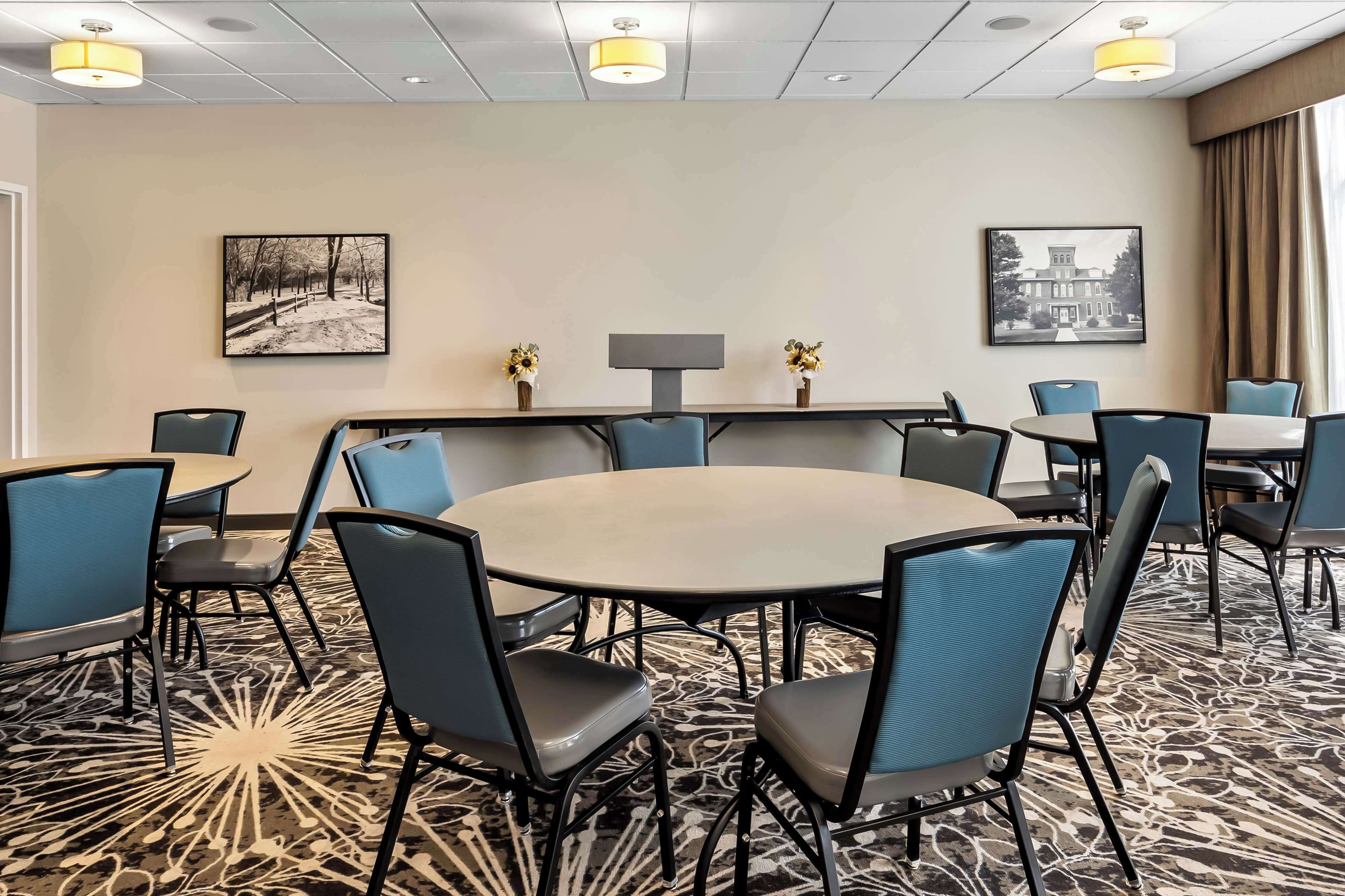 A conference room with a round table, blue chairs, and two wall-mounted lamps.