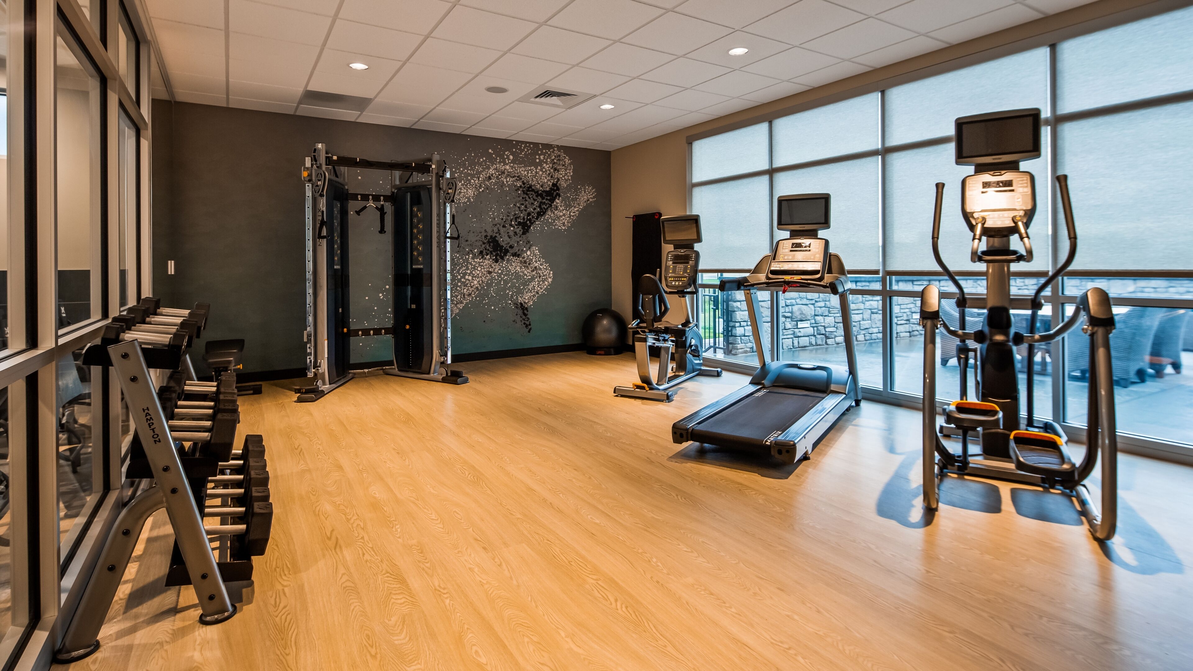 Un gimnasio con equipo cardiovascular, máquinas de pesas y un amplio ventanal con vistas al exterior.