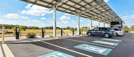 A gas station with electric vehicle charging stations, a covered canopy, and a bus labeled "TIGERS" in the background.