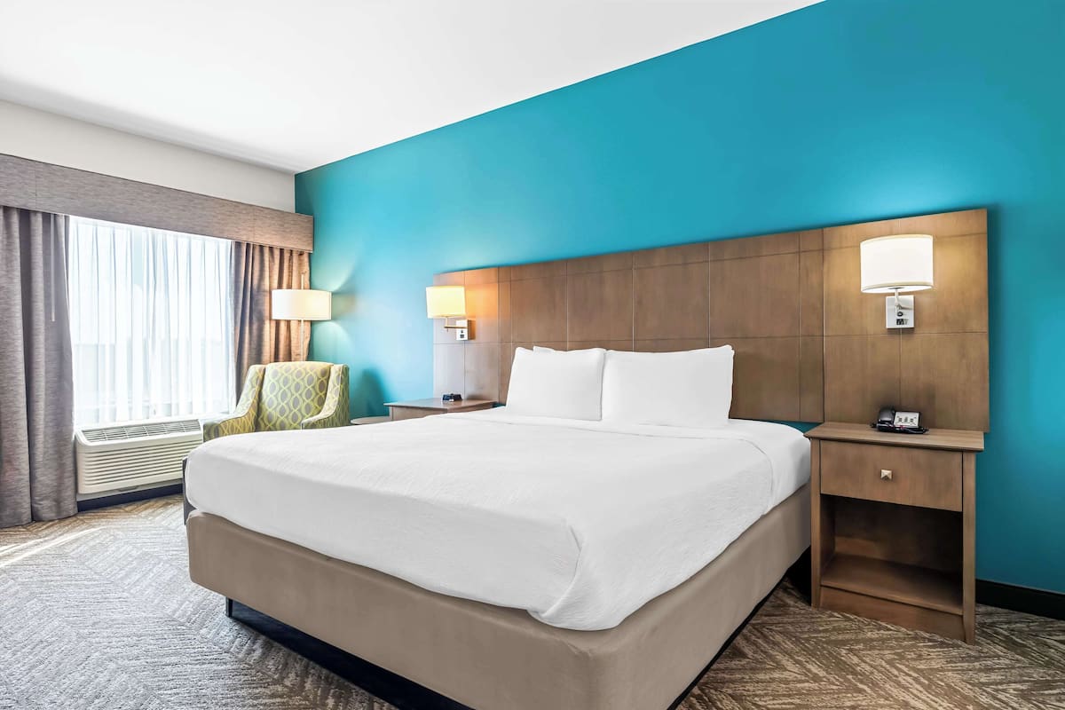 A hotel room with a large bed, two bedside tables with lamps, a chair, and a window with curtains.