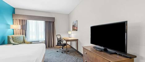 A hotel room with a bed, a desk, a chair, a television, and a lamp.