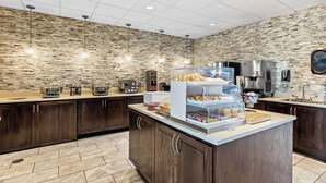 A modern kitchen with a stone wall backsplash, wooden cabinets, and a central island with food display. - Best Western Plus Bolivar Hotel & Suites (Bolivar)