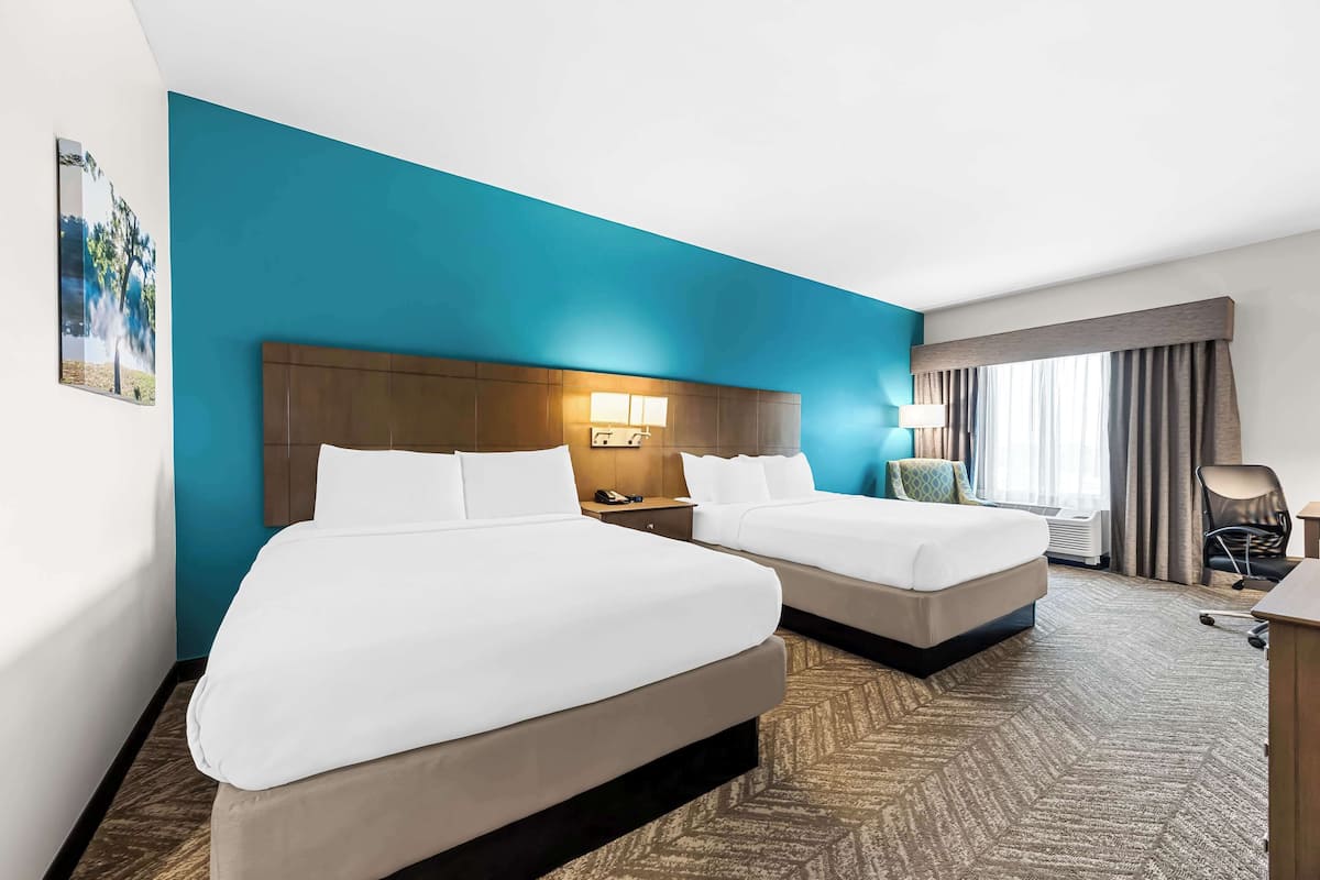 A hotel room with two beds, a nightstand, a desk, and a window with curtains.