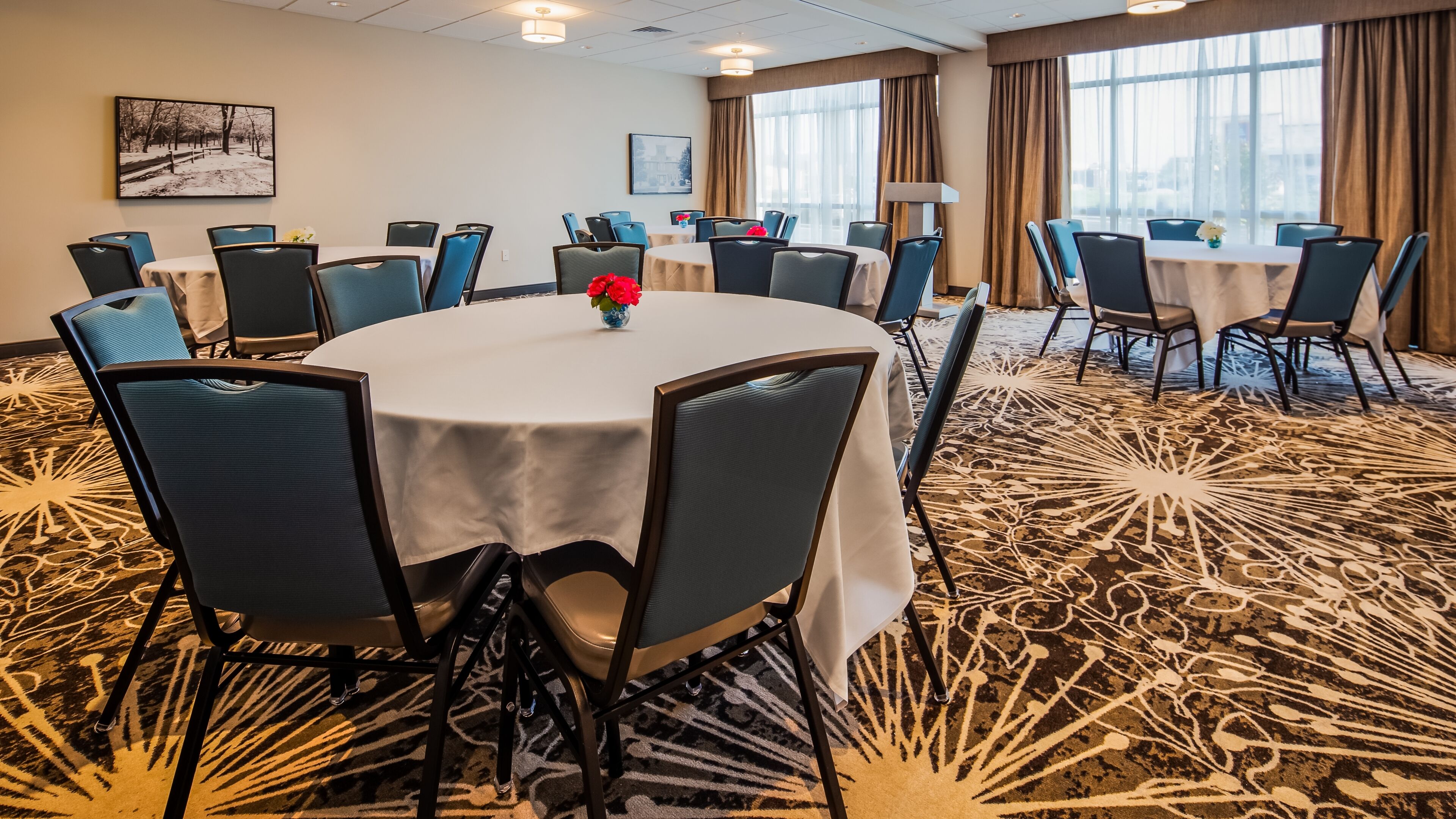 A conference room with round tables, chairs, and a carpeted floor.
