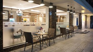 An outdoor seating area with wicker chairs and tables, a glass partition with a menu display, and pendant lighting. - Cityview Residence (Si Racha)