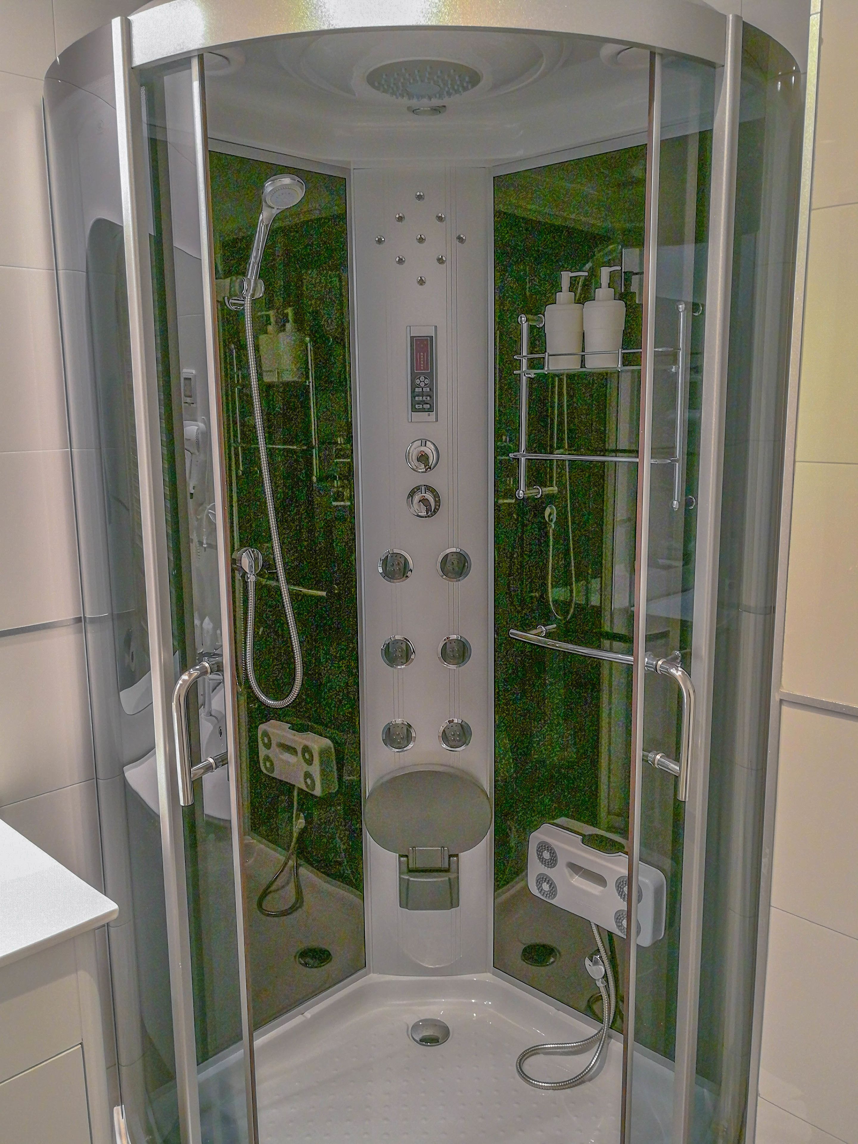 Un box de ducha moderno, con paredes de vidrio, múltiples cabezales, un panel de control y un asiento integrado.