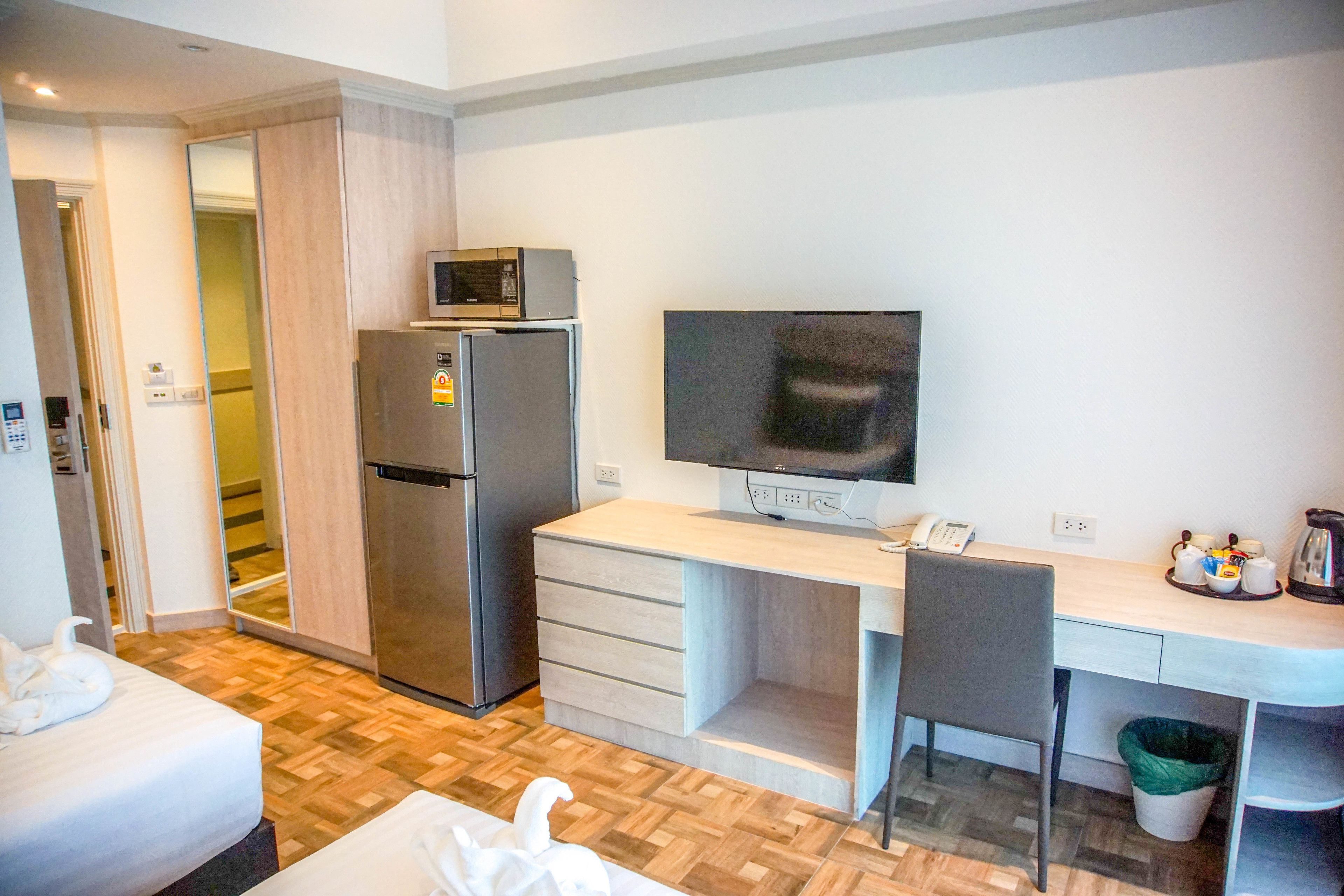 A compact hotel room with a bed, a kitchenette, a desk with a computer, and a TV.