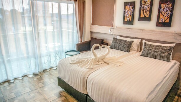 A hotel room with a large bed, a small table, a chair, and a window with curtains. - Cityview Residence (Si Racha)