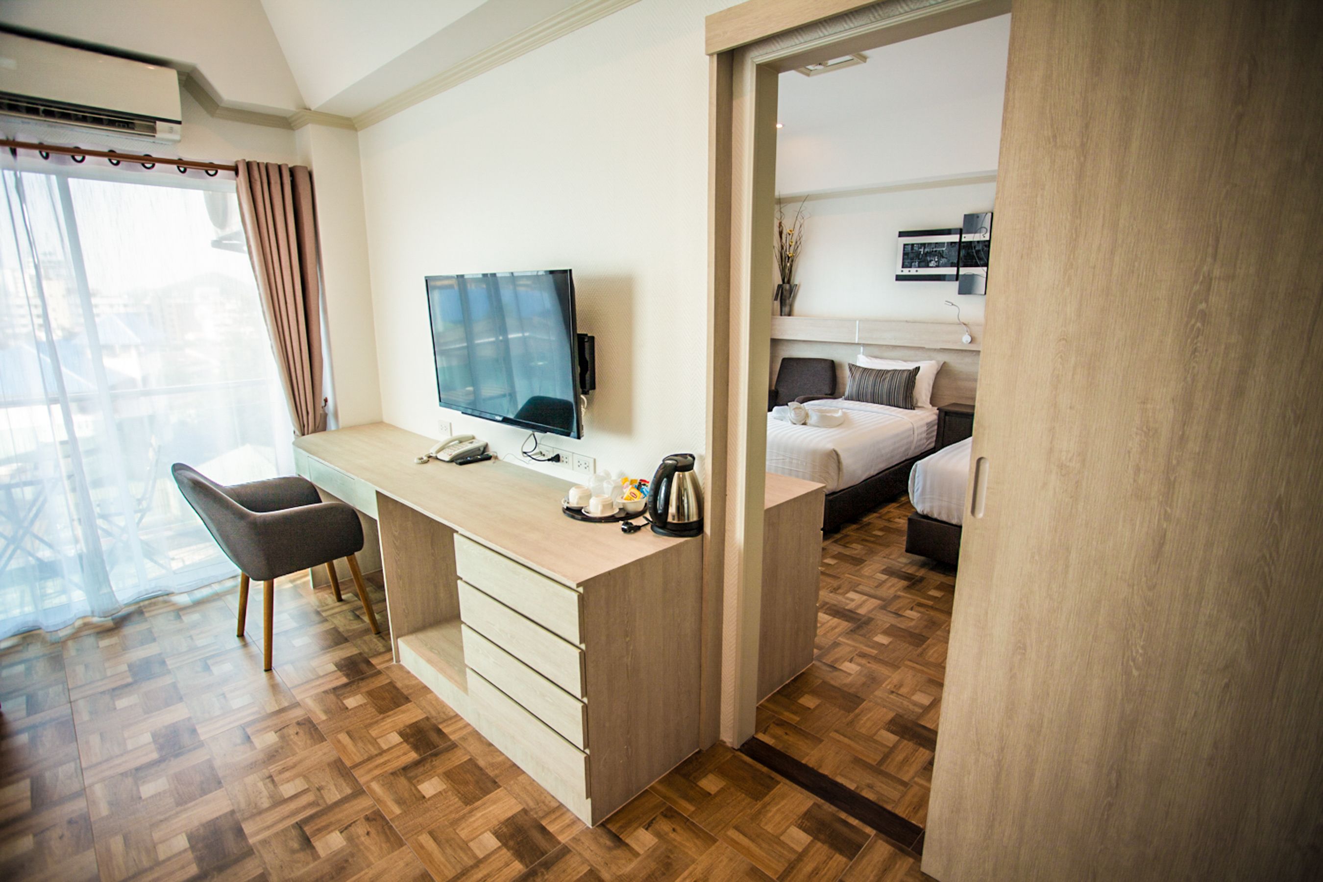 A hotel room with a wooden desk, a television, a chair, a bed, and a view through a window.