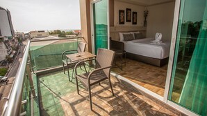 A balcony with a table and chairs, a bed with a white mattress and pillows, and a view of the cityscape. - Cityview Residence (Si Racha)