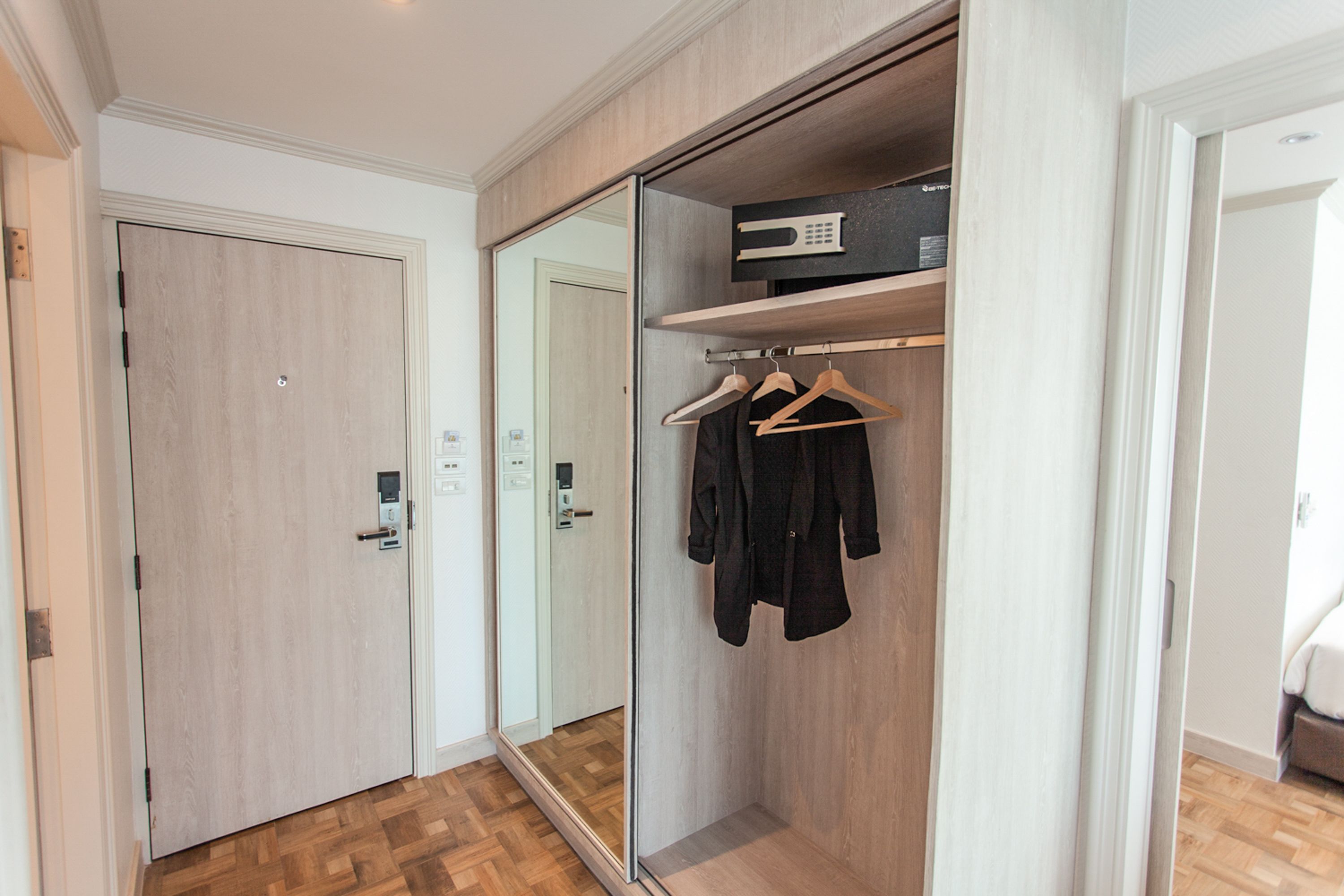 A modern room with a wooden floor, a mirrored closet with a hanging rack, and a small shelf with a black box.