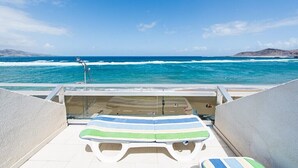 A balcony with a view of the ocean, a lounge area with striped cushions, and a railing.