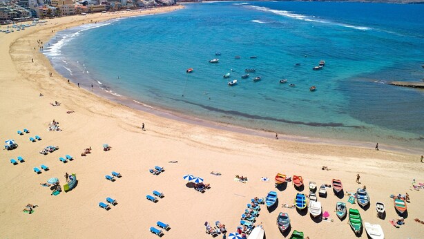 A beach with numerous boats and people.