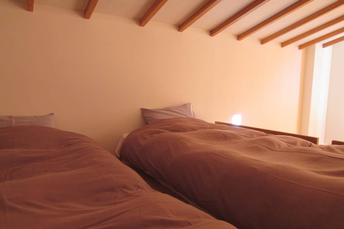 A bedroom with two beds, wooden headboards, and a window providing natural light.