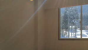 A room with tatami mats, a low wooden table with a teapot and cups, and a large window with a view of snow-covered trees. - Lodge Nakajima (Nozawaonsen)