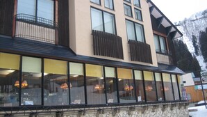 A multi-story building with large windows, stone facade, and balconies. - Lodge Nakajima (Nozawaonsen)