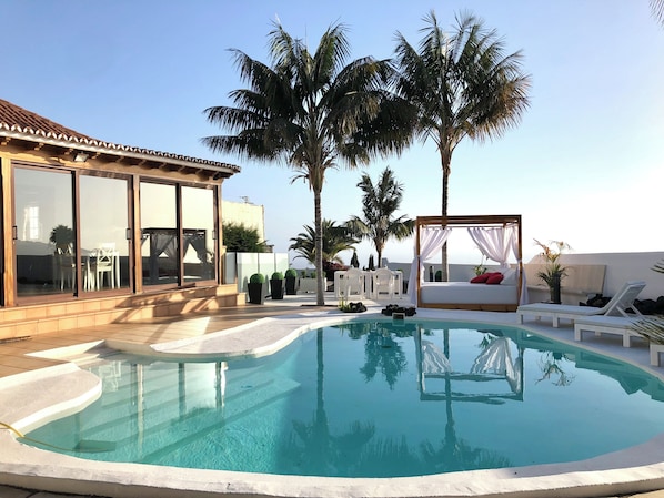 A swimming pool with a glass enclosure, a bed with a canopy, and palm trees.