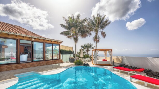 Une piscine bordée de chaises longues rouges, une terrasse en bois et une vue sur l’océan.