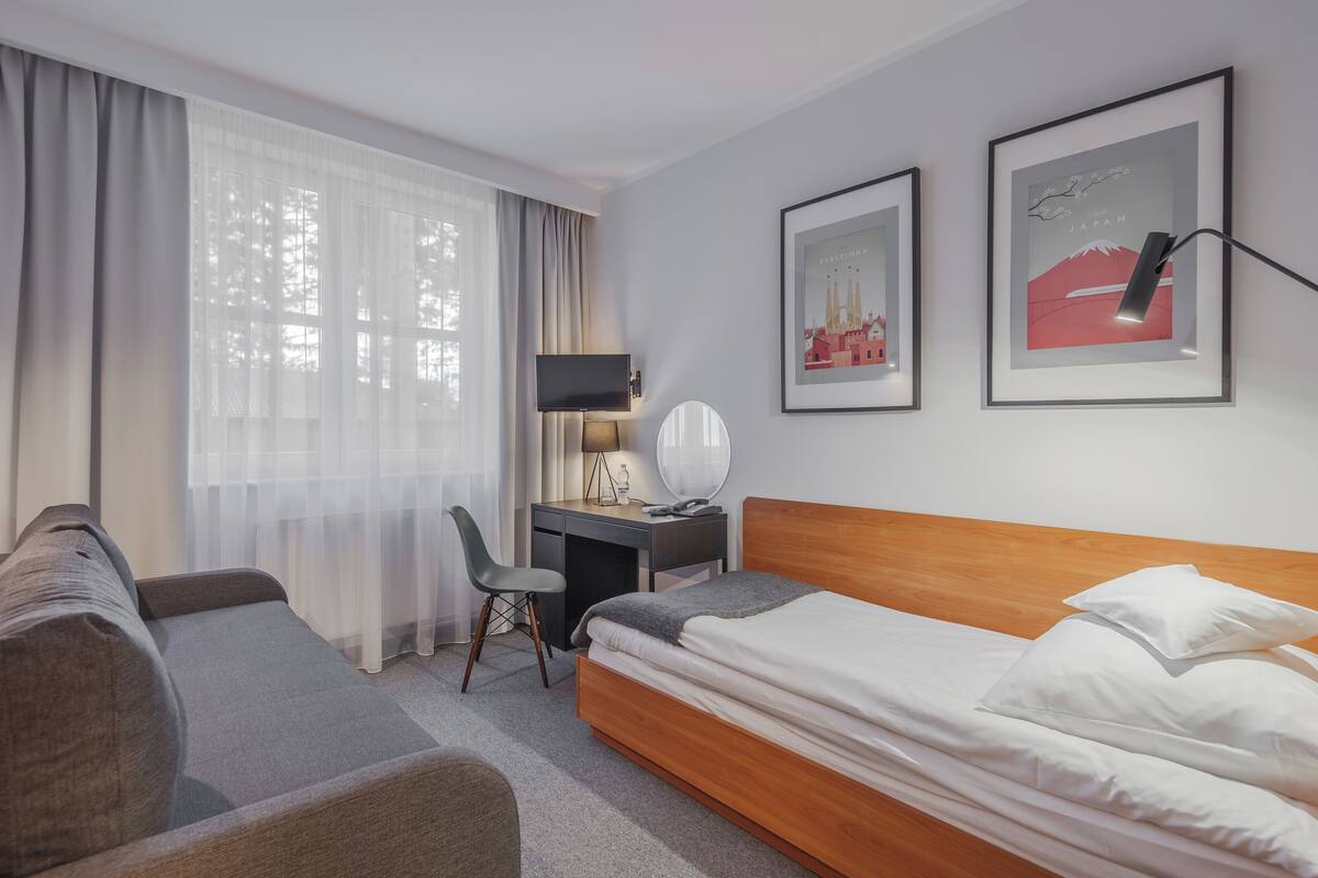 Ein Hotelzimmer mit einem Bett, einem Schreibtisch, einem Sessel und zwei gerahmten Bildern an der Wand.