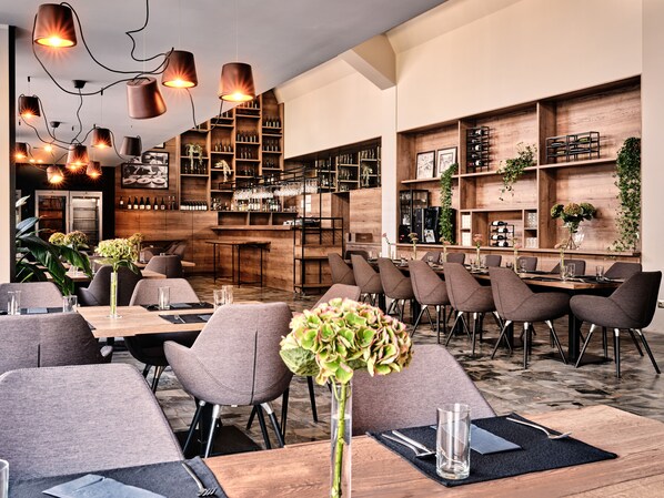 Un interior de restaurante moderno con estantes de madera, lámparas colgantes y mesas y sillas ordenadas.