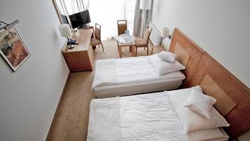 A hotel room with two beds, a desk, a chair, a TV, and a window with curtains.