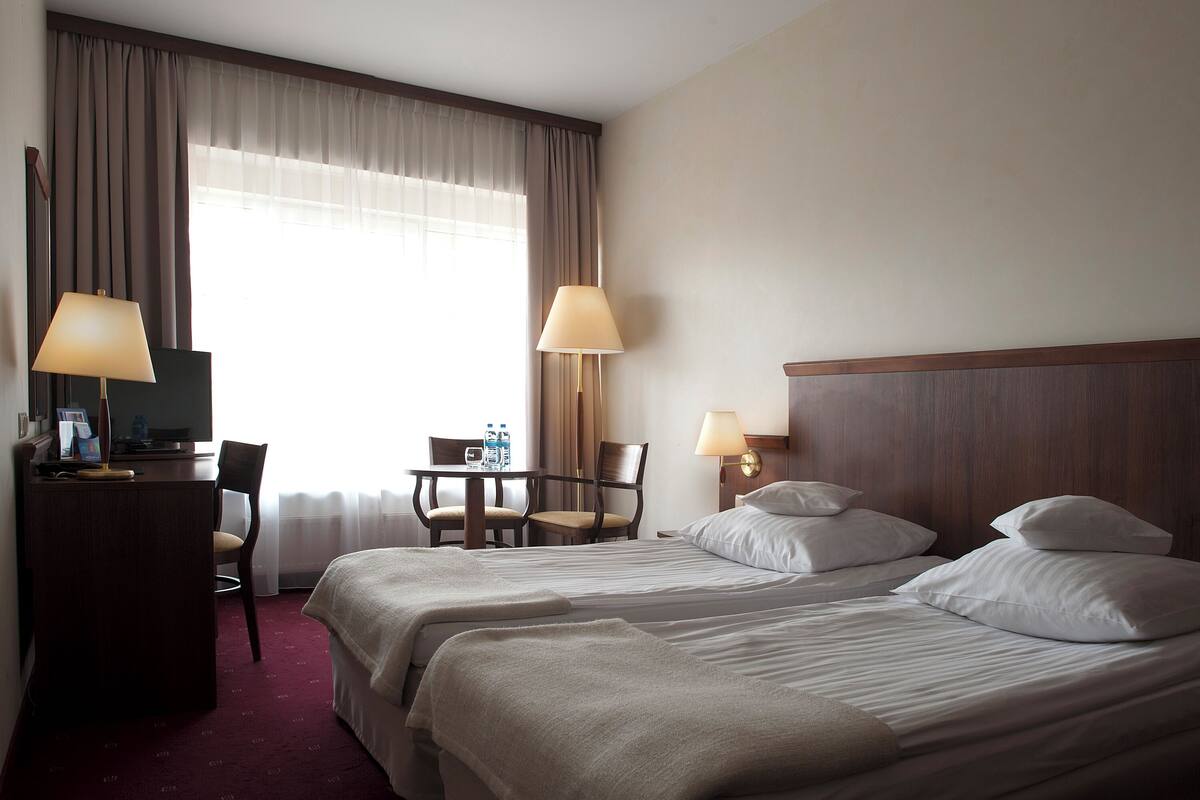 Ein Hotelzimmer mit zwei Betten, einem Schreibtisch, Stühlen, Lampen und einem Fernseher.