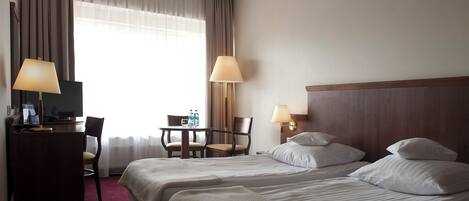 Habitación de hotel con dos camas, un escritorio, sillas, lámparas y un televisor.