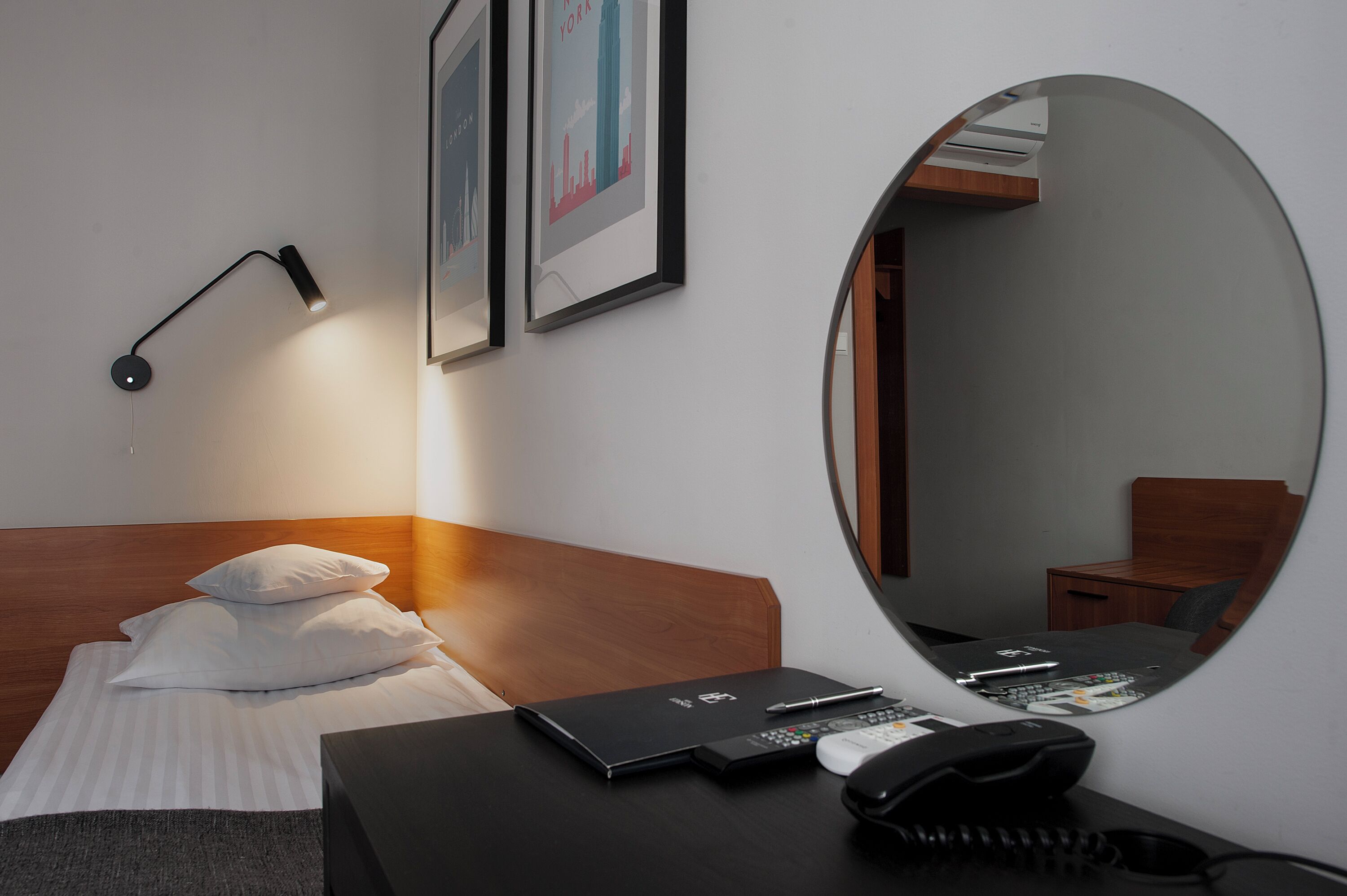 Ein Hotelzimmer mit einem Bett, einem Schreibtisch, einem Laptop, einem Telefon und einem Spiegel.