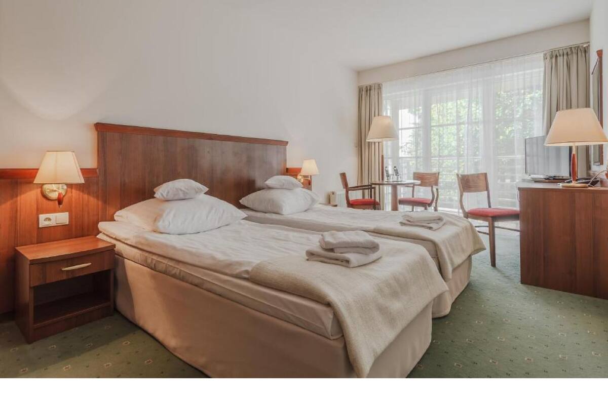 Ein Hotelzimmer mit zwei Betten, einem Schreibtisch, einem Stuhl und einem Fenster mit Vorhängen.