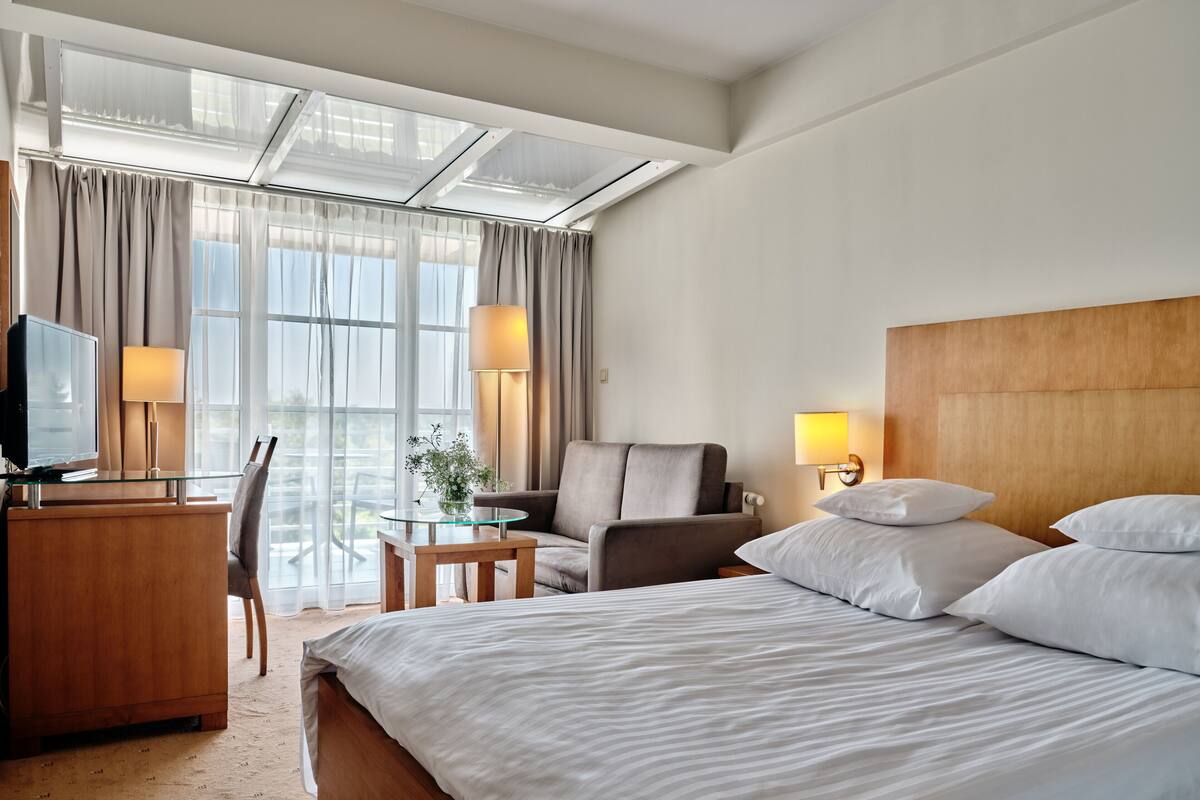 Ein Hotelzimmer mit Bett, Schreibtisch mit Fernseher, Stuhl, Lampe und einem Fenster mit Vorhängen.