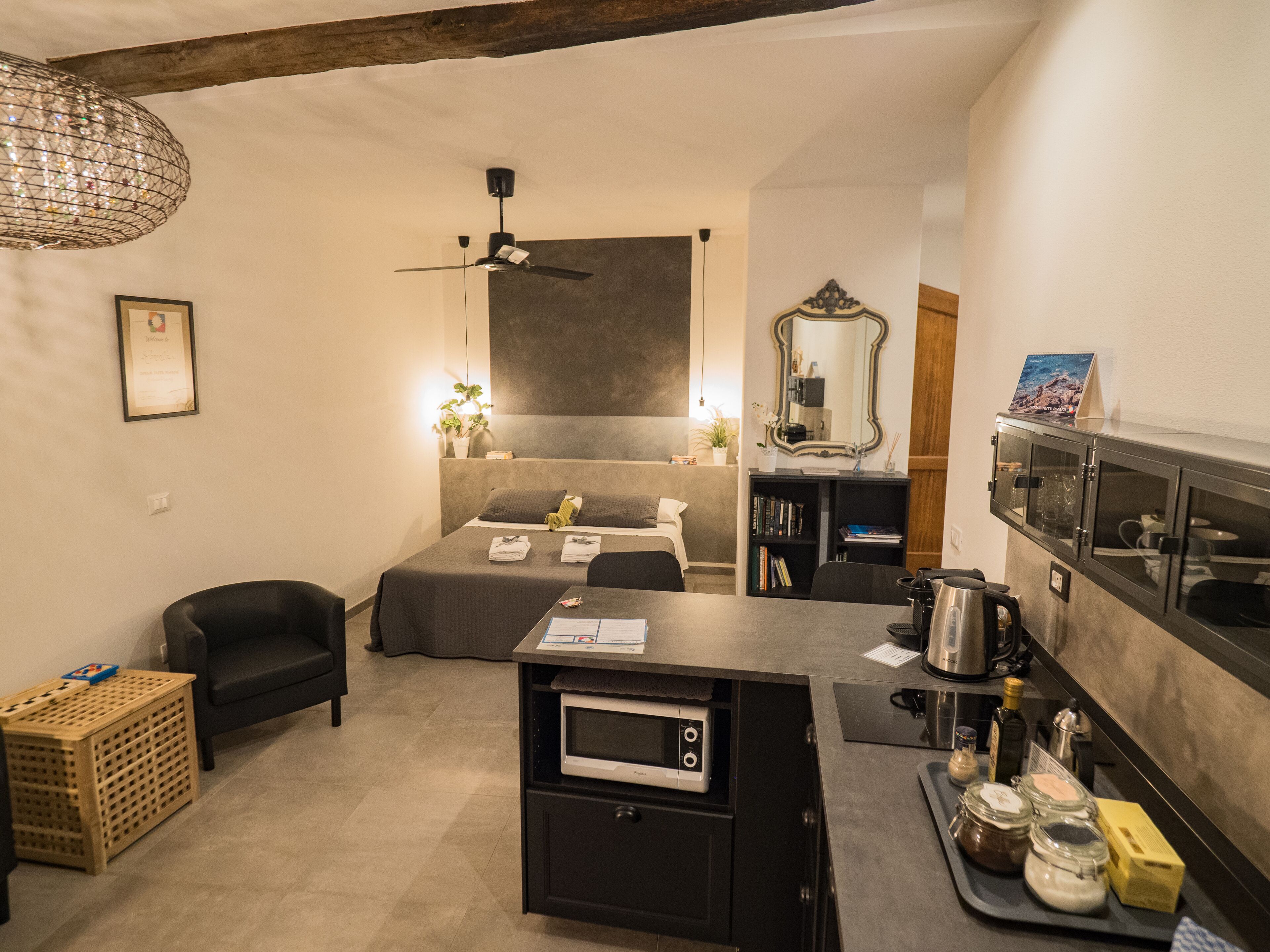 A compact hotel room with a bed, a small kitchenette, a seating area, and a mirror.