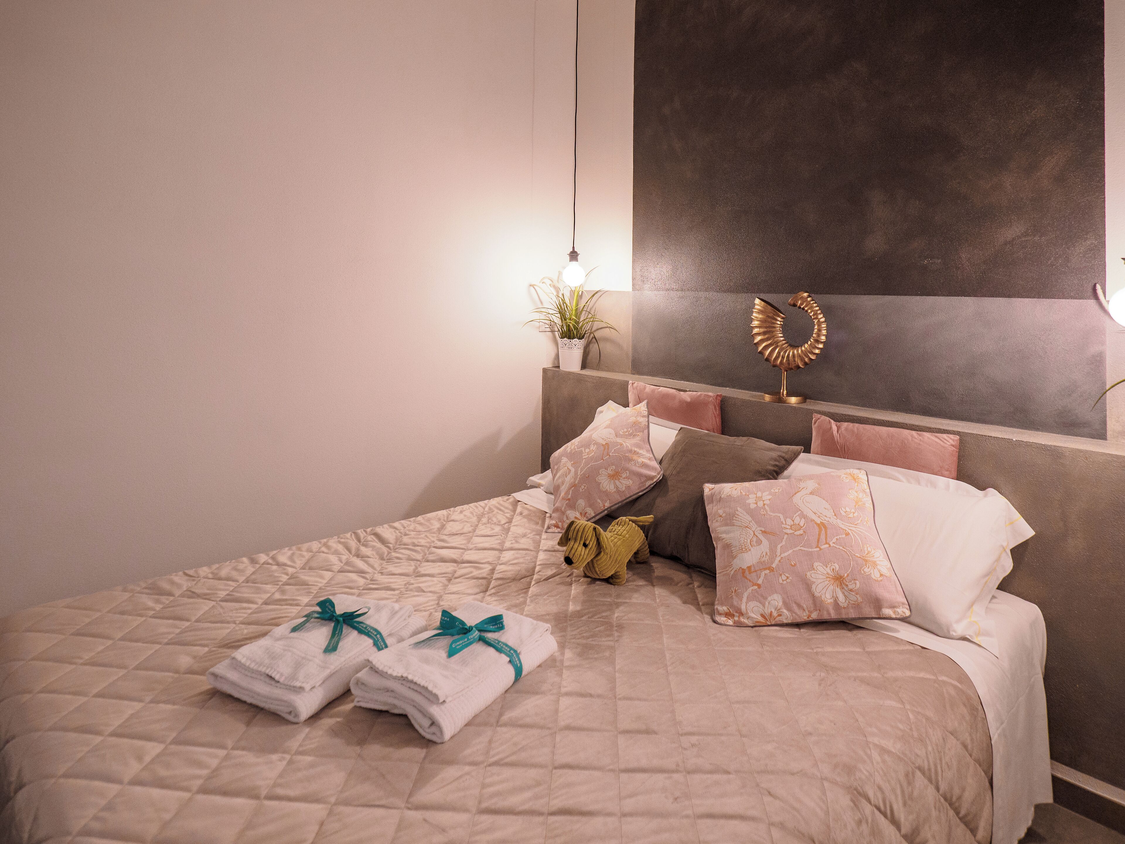 A neatly made bed with a quilted cover, several pillows, and folded towels with green ribbons.