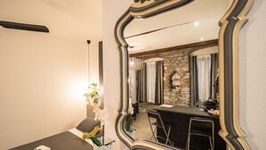 A room with a large mirror, a small table with towels, a potted orchid, and a stone wall with a sewing machine. - Camaella Luxury Studio (Vernazza)