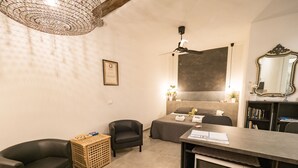 A compact hotel room with a bed, a desk, a chair, a small kitchenette, and a ceiling fan. - Camaella Luxury Studio (Vernazza)