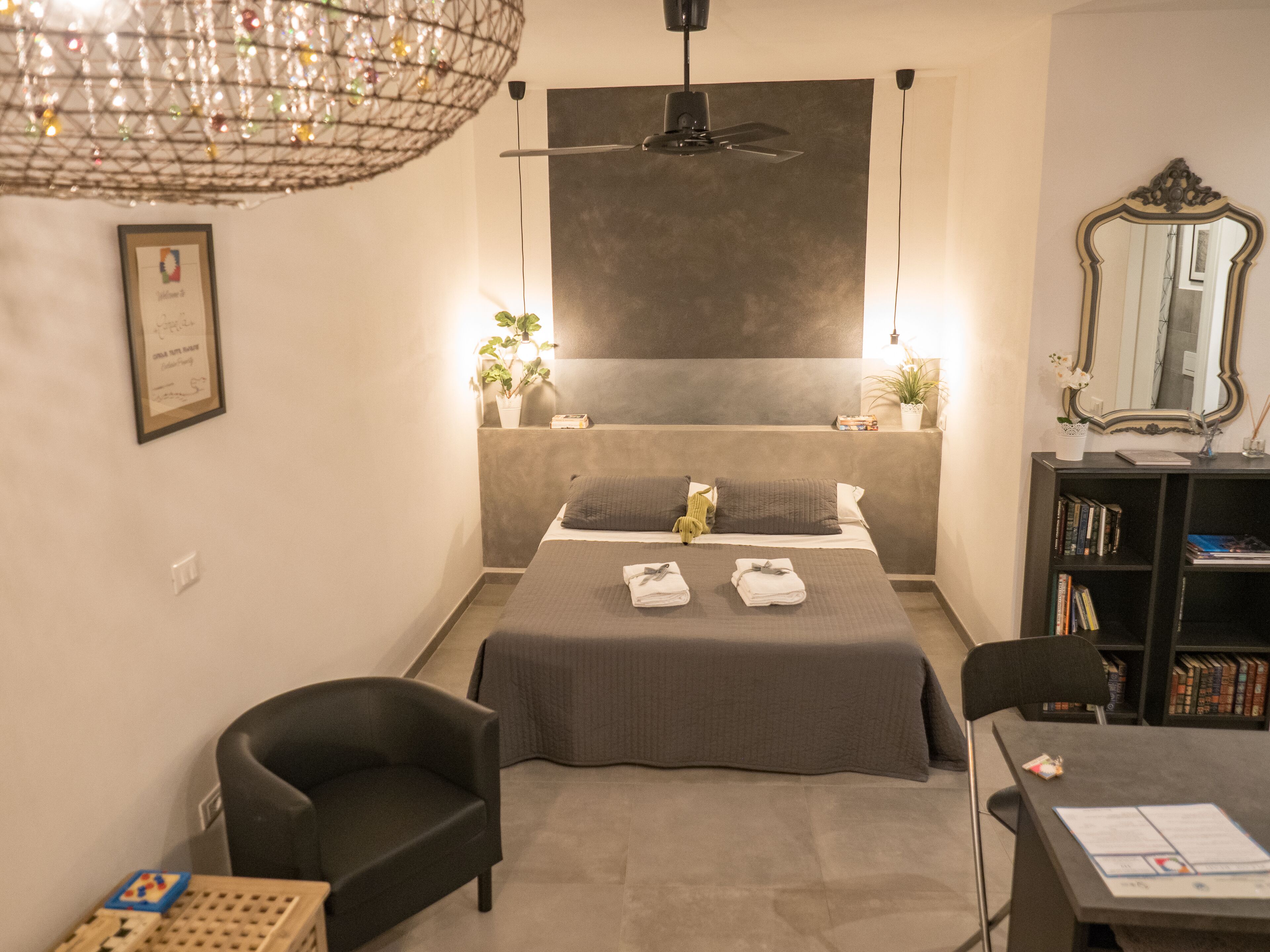 A modern bedroom with a large bed, bedside tables, a desk, a chair, a bookshelf, and a ceiling fan.