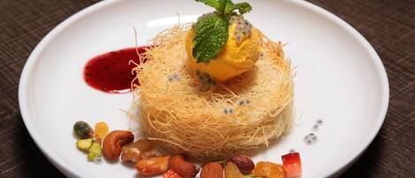 A dessert on a white plate with a red sauce, a mint leaf, and various nuts.