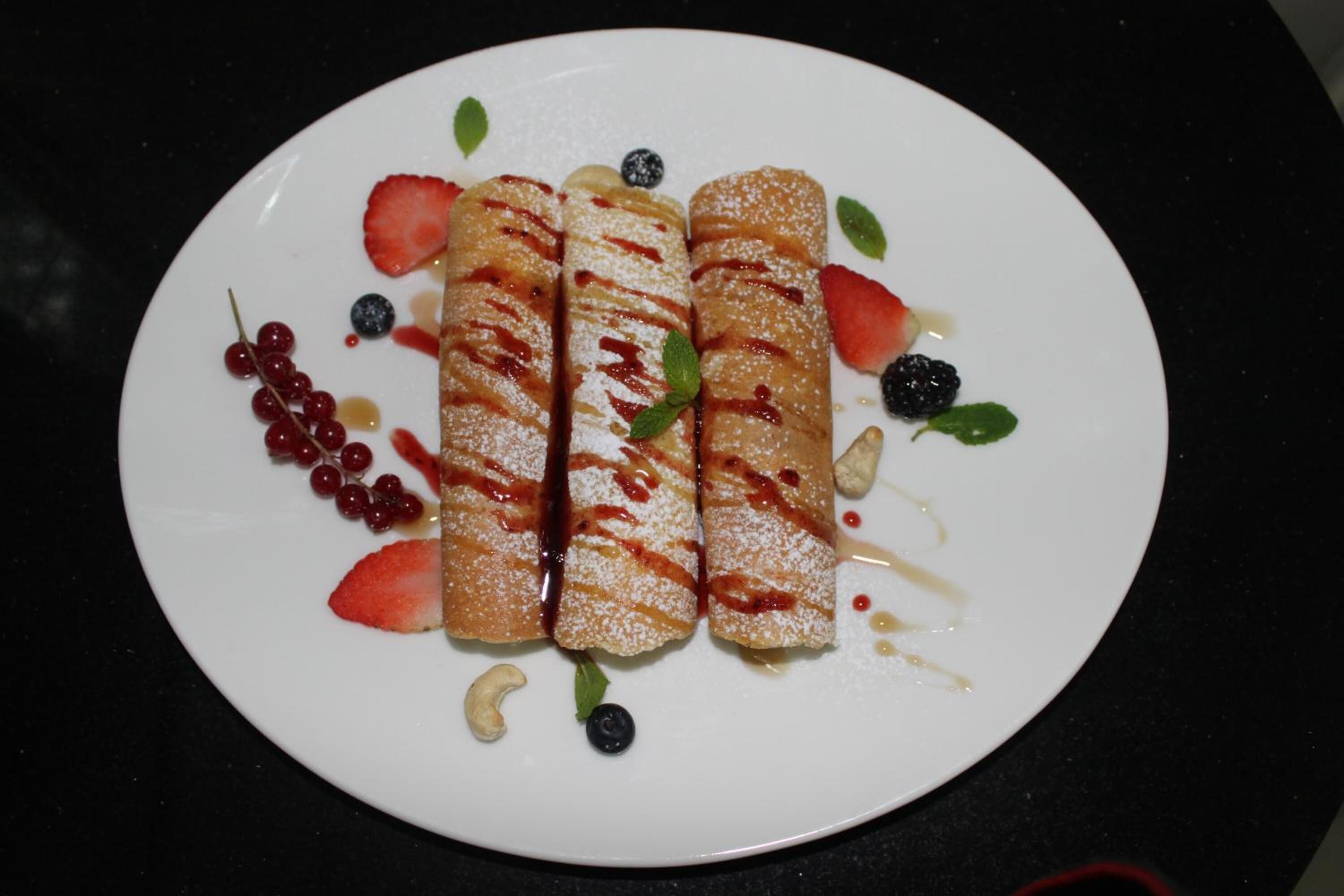 A plate of rolled pastries with fruit and powdered sugar.