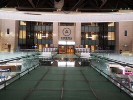 An interior view of the Aerotel Airport Transit Hotel with a central atrium, glass railings, and a prominent 'A' logo on the wall.