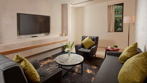 Una sala moderna con un televisor de pantalla plana montado en la pared, una mesa redonda de centro con un jarrón de flores y un sofá con cojines verdes.