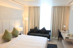 A hotel room with a bed, a sofa, a desk, and a lamp.