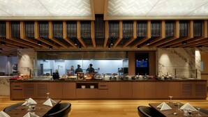 Un restaurante moderno con una barra larga, paneles de madera, detalles de mármol y un techo alto con un diseño geométrico.