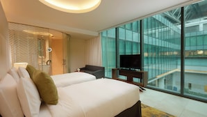 Habitación de hotel moderna con dos camas, televisión y grandes ventanas que ofrecen vistas al interior del edificio.