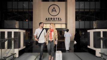 La entrada del Hotel Aerotel Transit Airport, con un diseño moderno, que destaca un logotipo prominente y un frente de vidrio.