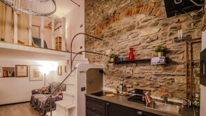 A modern kitchen with a stone wall, wooden staircase, and a small dining area with a floral sofa. - Petrella's Point Studio with AC (Vernazza)